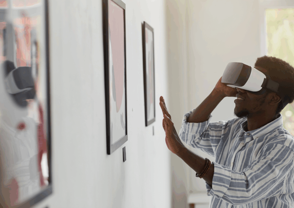 A young man wearing VR goggles stands in front of a painting that he appears to be exploring using his hand and the VR equipment